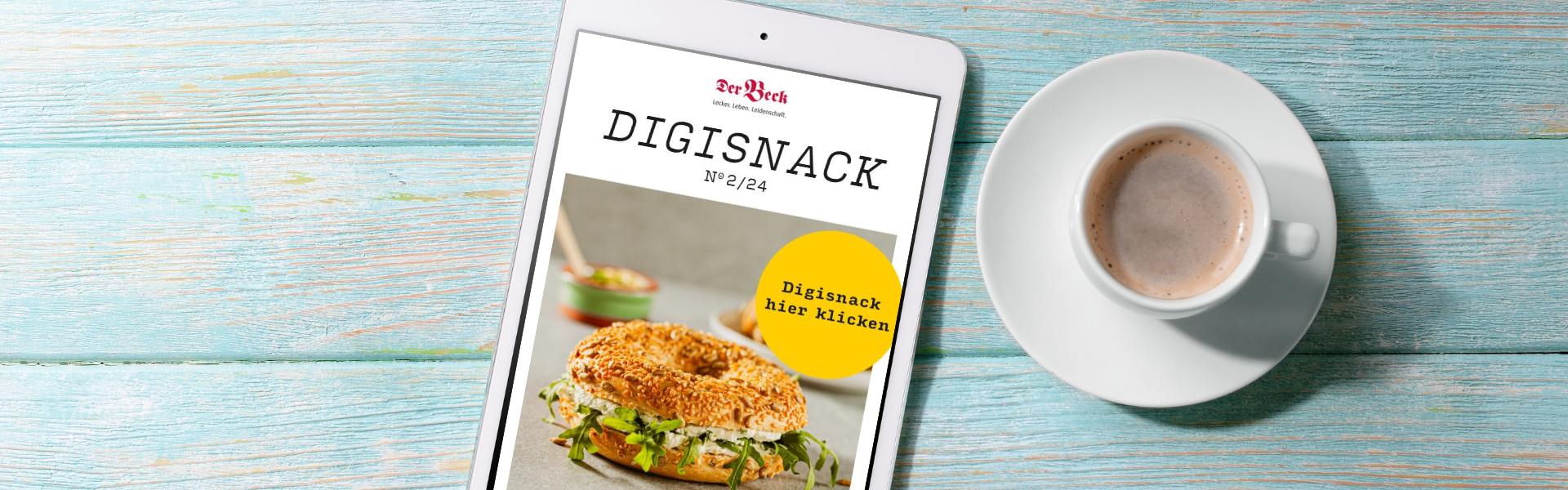 Ein auf einem weißen Tablet geöffneter DigiSnack  zusammen mit einer Tasse Kaffee auf  blauem Holzuntergrund